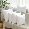 A collection of white cotton-filled decorative throw pillows arranged on a light-colored sofa near a window.