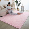A pink fluffy rug is placed on a light wood floor in a living room setting.