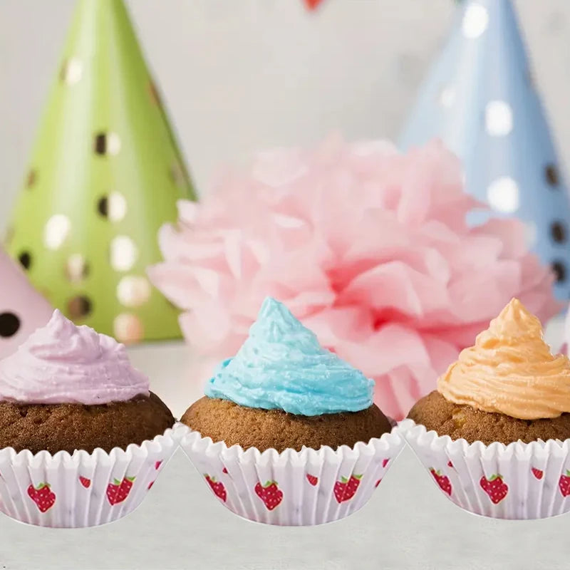 Three cupcakes with pastel colored frosting are displayed in pink and white strawberry pattern baking cups.