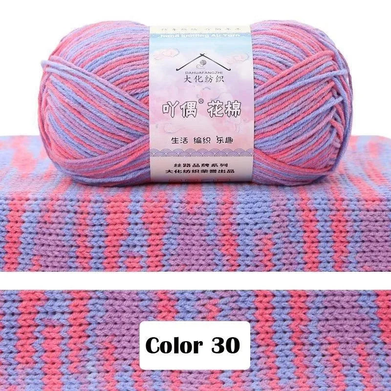 A ball of pink and purple gradient yarn is displayed on a knitted fabric background.