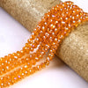 A strand of faceted orange glass beads is shown draped over a cylindrical object.