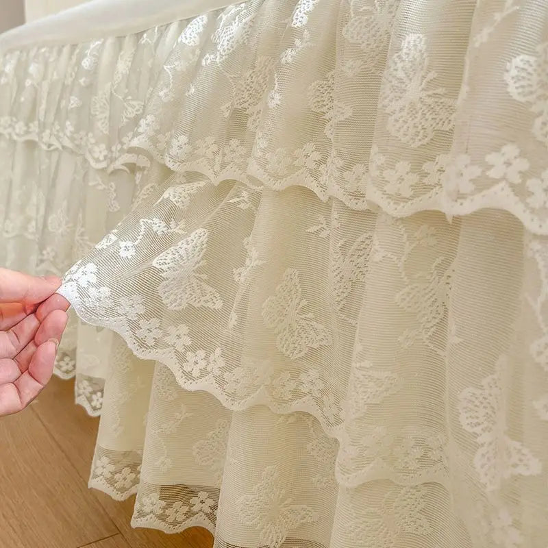 A cream colored lace ruffled bed skirt set with delicate floral embroidery.