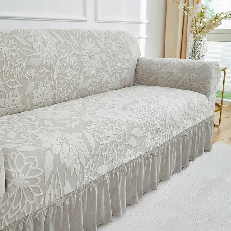 A light beige jacquard stretch sofa cover featuring a floral pattern and gathered ruffle trim.