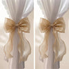 A pair of sheer beige ribbon bow curtain tiebacks displayed against a white fabric background.