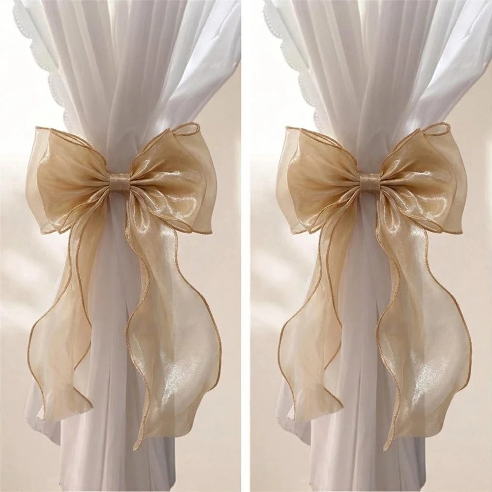 A pair of sheer beige ribbon bow curtain tiebacks displayed against a white fabric background.