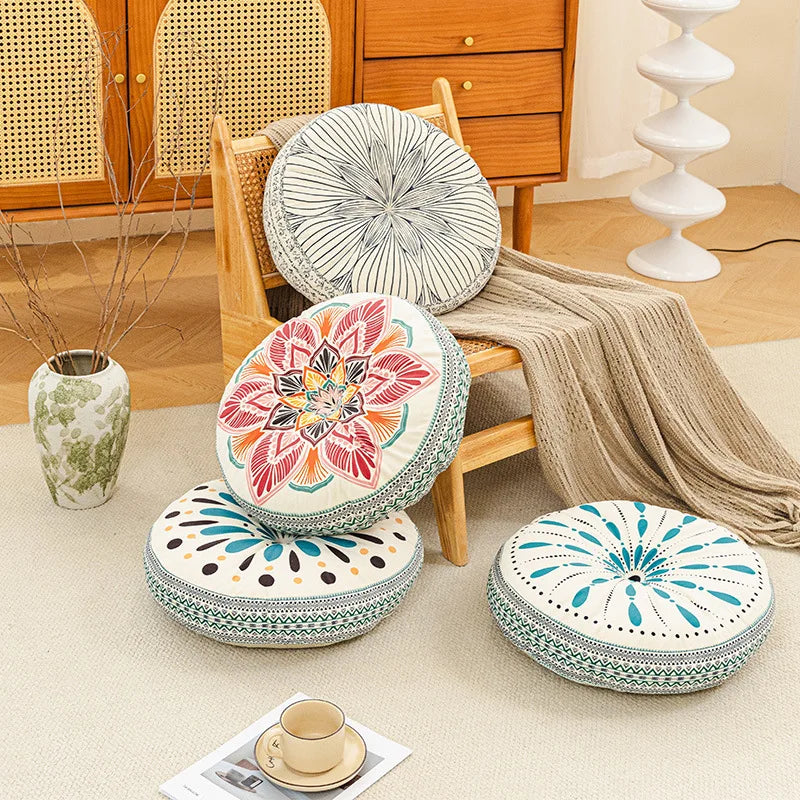 A collection of round, patterned cushions and a woven textile displayed on a light rug next to wooden furniture.
