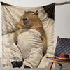 A brown marmot is resting on a light-colored flannel blanket, with dark fabric draped around it.