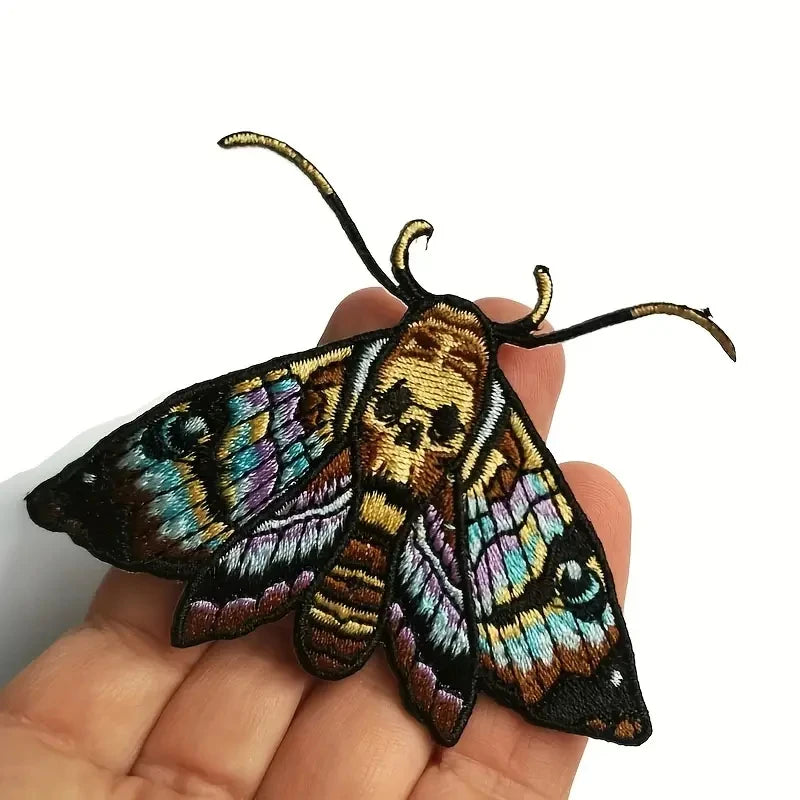 A detailed embroidered patch of a colorful moth with intricate patterns on a hand.