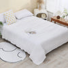 A white pure cotton gauze throw blanket is neatly folded on a bed with yellow patterned pillows and natural decor.