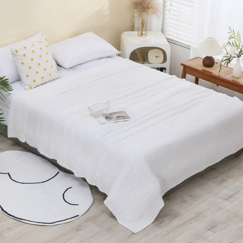 A white pure cotton gauze throw blanket is neatly folded on a bed with yellow patterned pillows and natural decor.