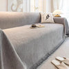 A light gray elegant jacquard sofa cover blanket draped over a sofa with a decorative pillow and a cup on the surface.