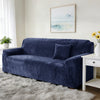 A deep navy stretch velvet sofa slipcover with a throw pillow on a light rug and framed artwork.
