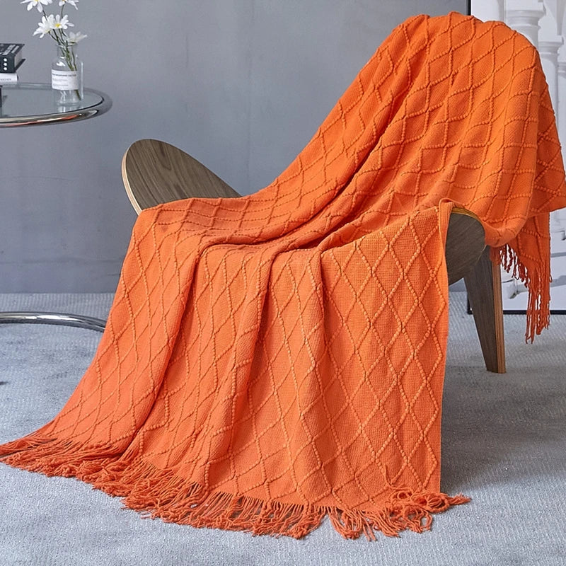 A vibrant orange oversized knitted tassel throw blanket draped over a wooden chair.
