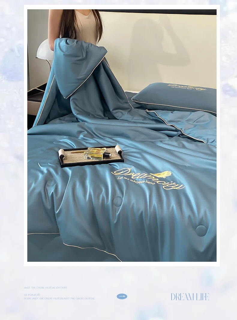 A teal ultra-soft ice silk fiber summer quilt draped on a bed, with a pillow and a wooden tray visible.