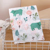 A white muslin swaddle blanket featuring green and pink botanical prints, including bears and flowers.
