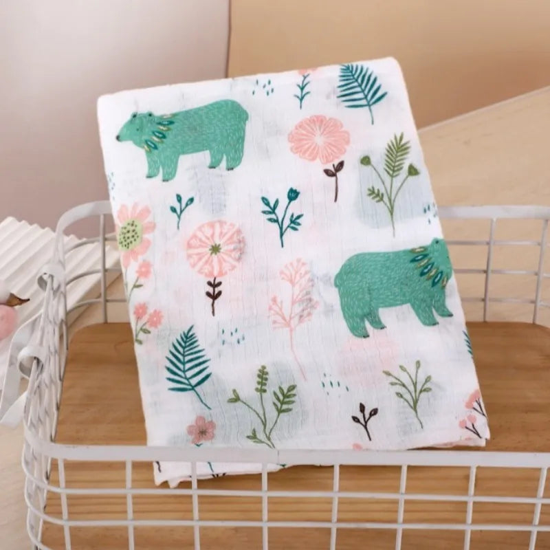 A white muslin swaddle blanket featuring green and pink botanical prints, including bears and flowers.