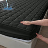 A hand is touching a black quilted waterproof mattress protector on a bed.