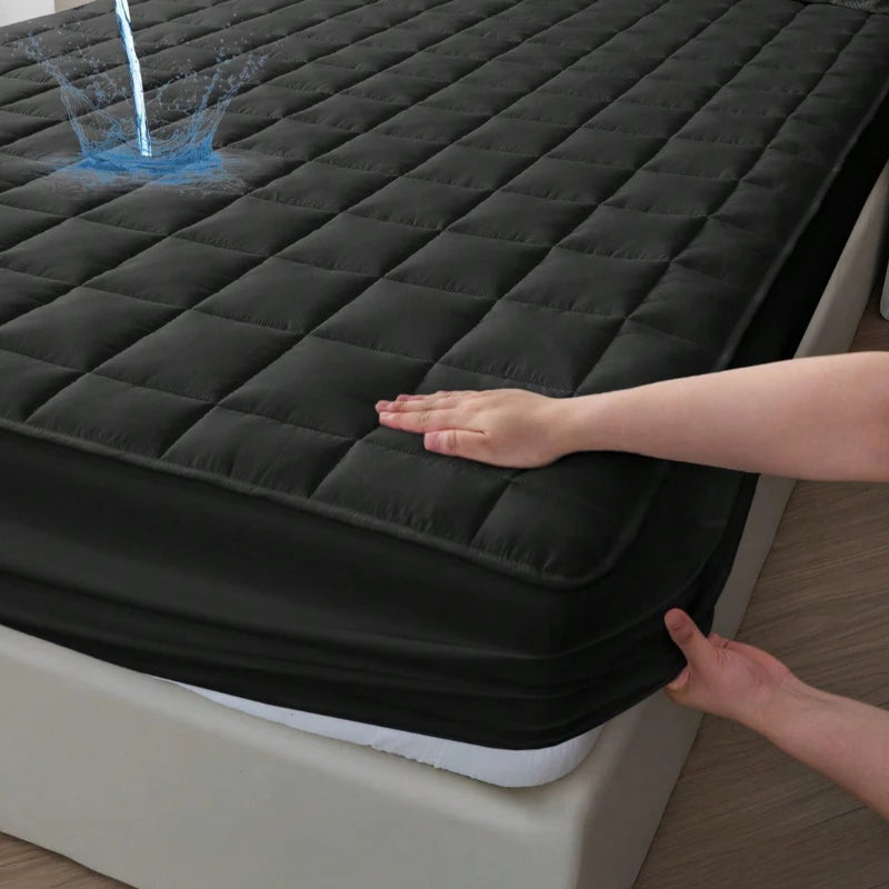 A hand is touching a black quilted waterproof mattress protector on a bed.