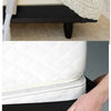A close-up of a white knitted box spring protector cover being placed over a black box spring.