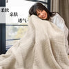 A woman smiling while wrapped in a beige, textured cotton gauze blanket.