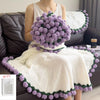 A woman is holding a handmade rose crochet blanket bouquet with purple and green accents on a white knitted garment.