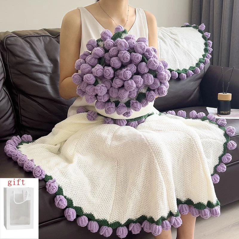 A woman is holding a handmade rose crochet blanket bouquet with purple and green accents on a white knitted garment.