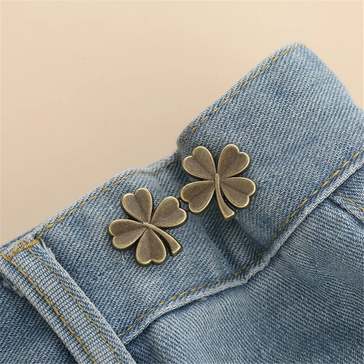 A pair of gold-toned clover button clips are fastened onto the fabric of a denim garment.