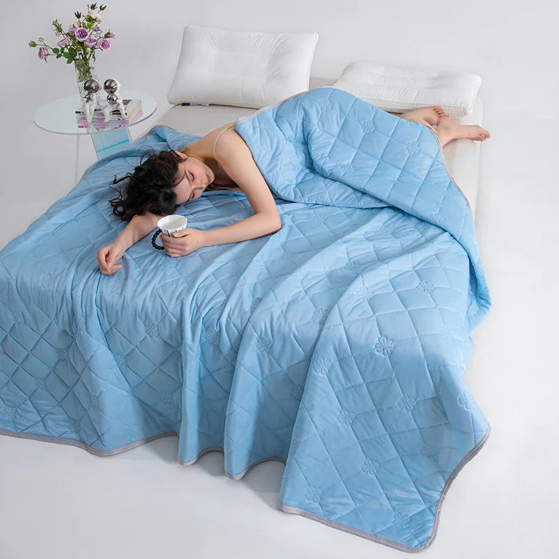 A woman is relaxing on a light blue quilted blanket indoors.