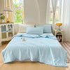 Light blue breathable waffle quilt spread on a bed in a bright room with sheer curtains.