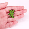 A hand holds a green plankton enamel brooch against a white background.