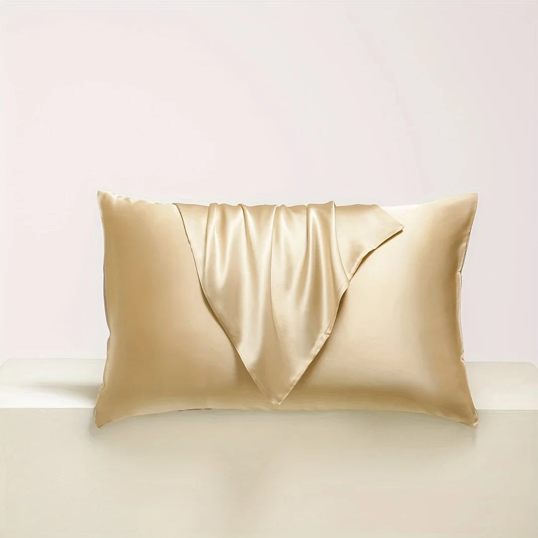 A golden satin pillowcase with draped fabric is shown resting on a light surface.