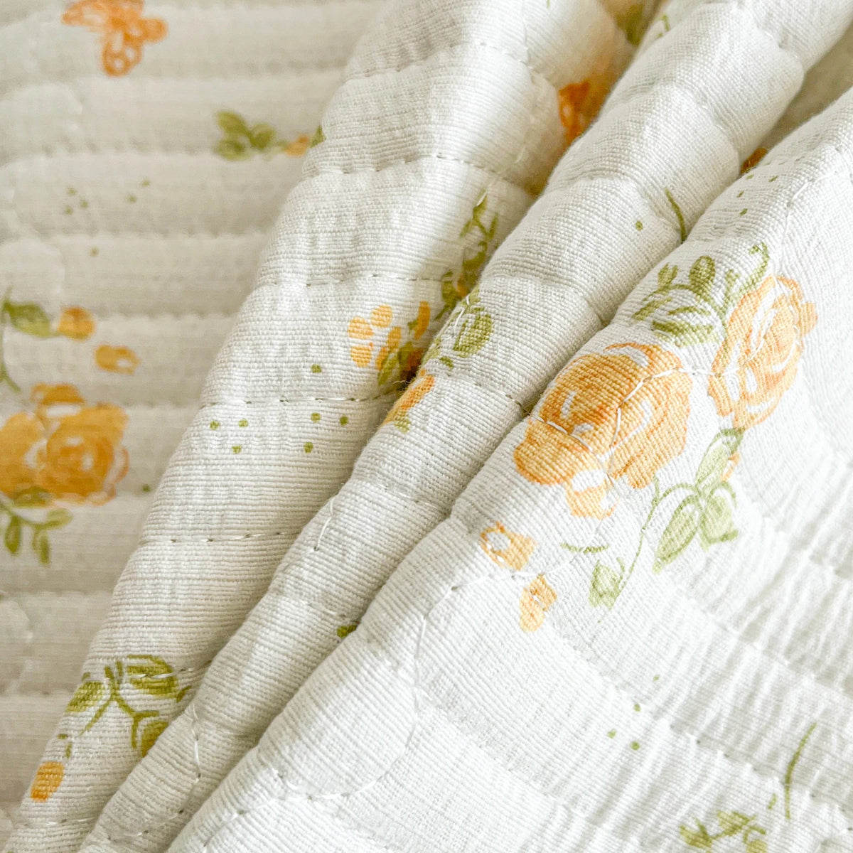 A close-up of a white quilted bedspread with delicate orange and green floral patterns.