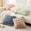 A collection of fluffy winter throw pillows in shades of pink, cream, and gray resting on a white sofa.