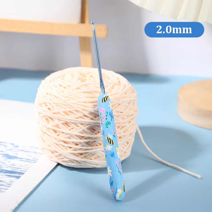 A single blue ergonomic crochet hook with a pink and yellow design is shown next to a ball of cream-colored yarn.