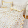 White floral quilted bedspread with yellow trim and matching pillows on a white wooden bed frame.