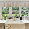 A bathroom vanity featuring a white sink and gold faucet with a rustic crochet half curtain above the mirror.