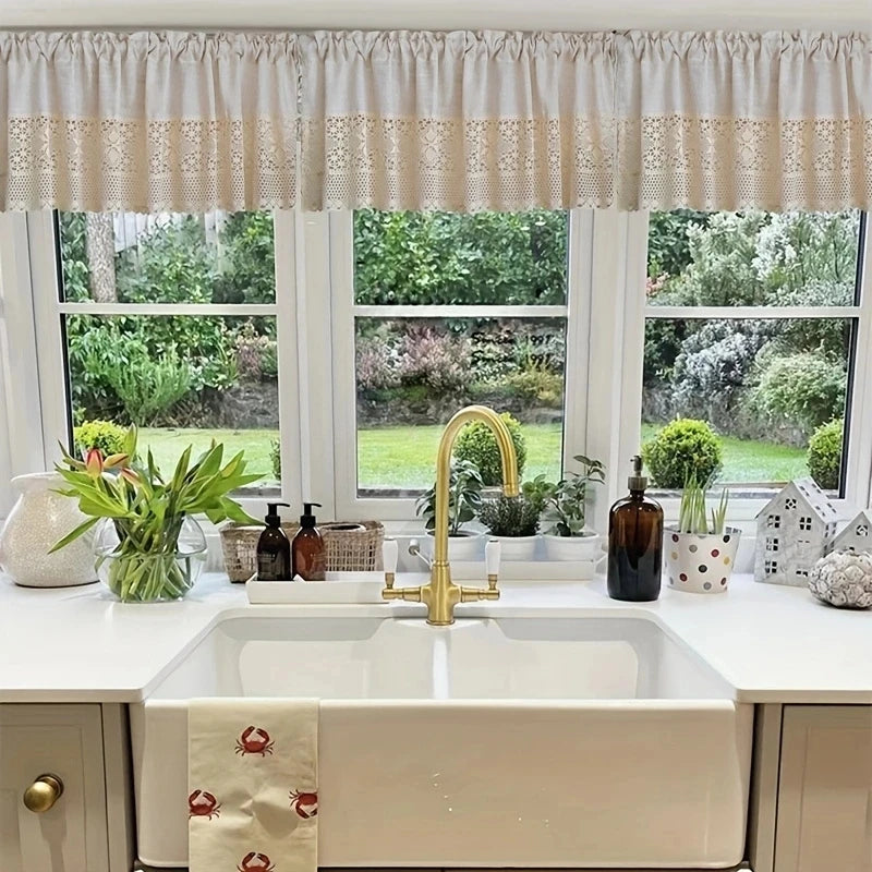 A bathroom vanity featuring a white sink and gold faucet with a rustic crochet half curtain above the mirror.