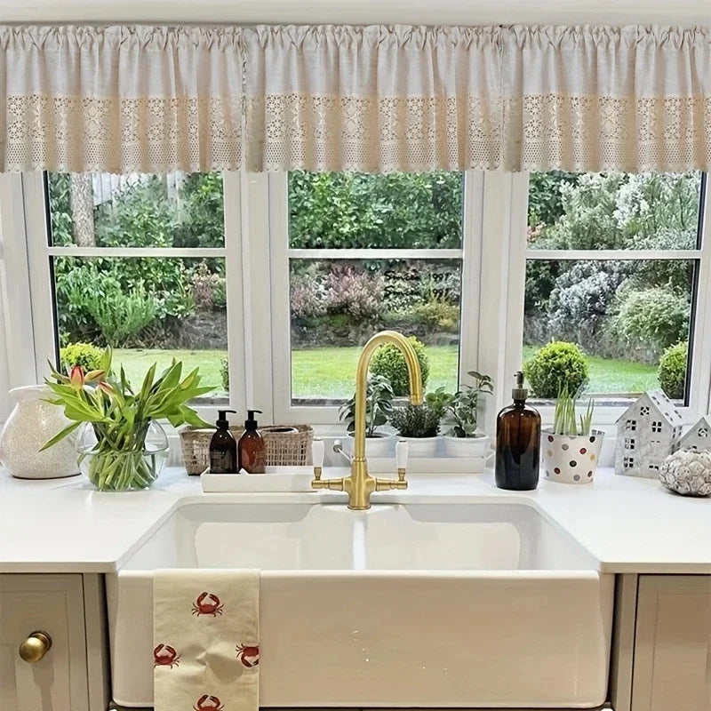 A bathroom vanity featuring a white sink and brass faucet under a sheer linen crochet half curtain.
