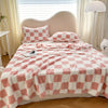 A pink and white checkered flannel blanket is spread on a bed with a headboard, featuring matching pillows.