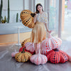 A woman stands next to various orange and black polka-dotted pumpkin plush cushions.