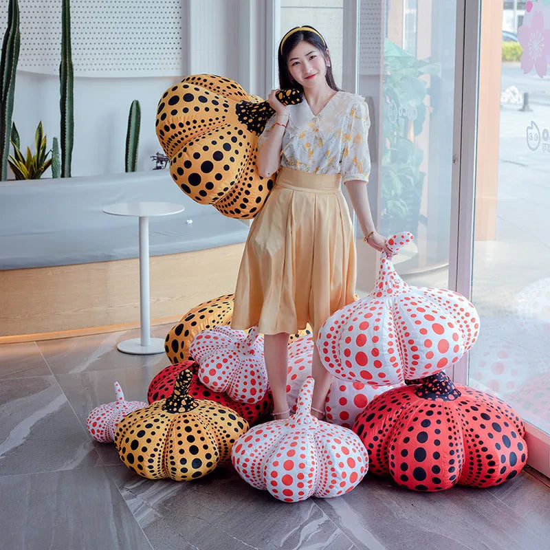A woman stands next to various orange and black polka-dotted pumpkin plush cushions.