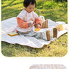 A baby is sitting on a pink play mat outdoors, interacting with food and toys.
