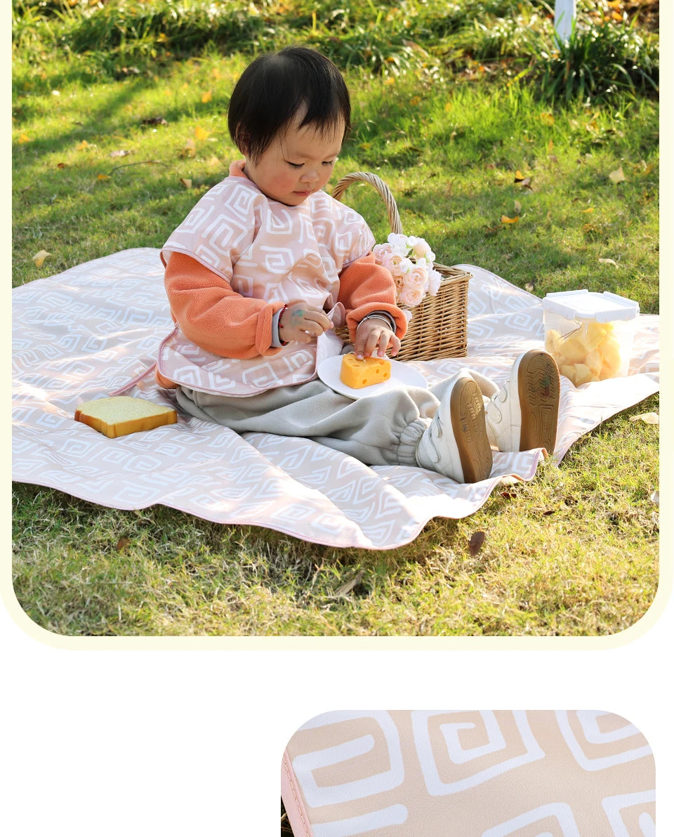 A baby is sitting on a pink play mat outdoors, interacting with food and toys.