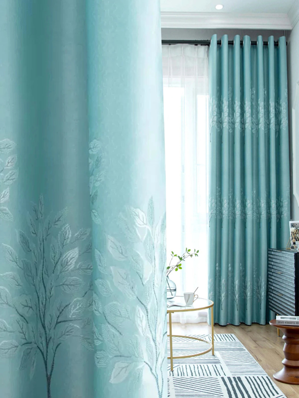 Light blue curtains featuring a white botanical design, shown next to sheer white curtains and a wooden floor.