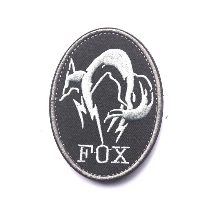 A black embroidered patch featuring a silver silhouette of a fox head with lightning bolts and the text FOX.
