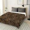 A luxurious leopard print flannel blanket spread across a bed with light gray pillows and wooden frame.