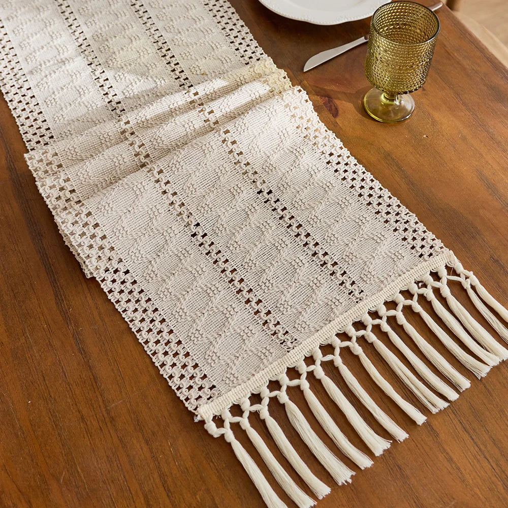 Beige boho hand-woven table runner with fringe detail on a wooden surface.