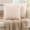 Two beige faux fur decorative pillowcases resting on a tan knitted throw blanket.