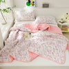 A pink and white quilted summer quilt set displayed on a white bed with pillows and a blanket.