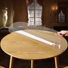 A round waterproof PVC tablecloth with a decorative print is displayed on a wooden table.